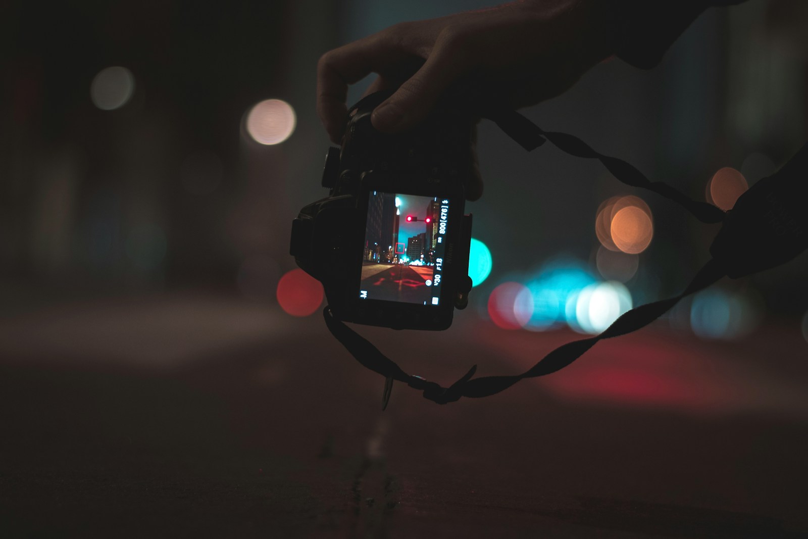 person holding black DSLR camera capturing photo of streets with bokeh lights